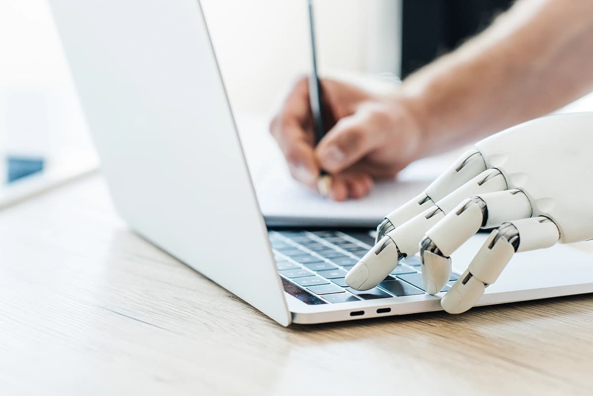 Close-up view of robotic arm using laptop and human hand