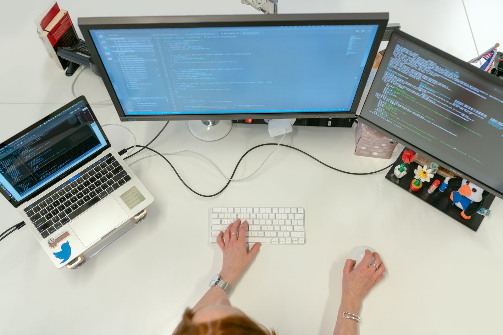 Overhead view of an engineer working with code across a laptop and two monitors