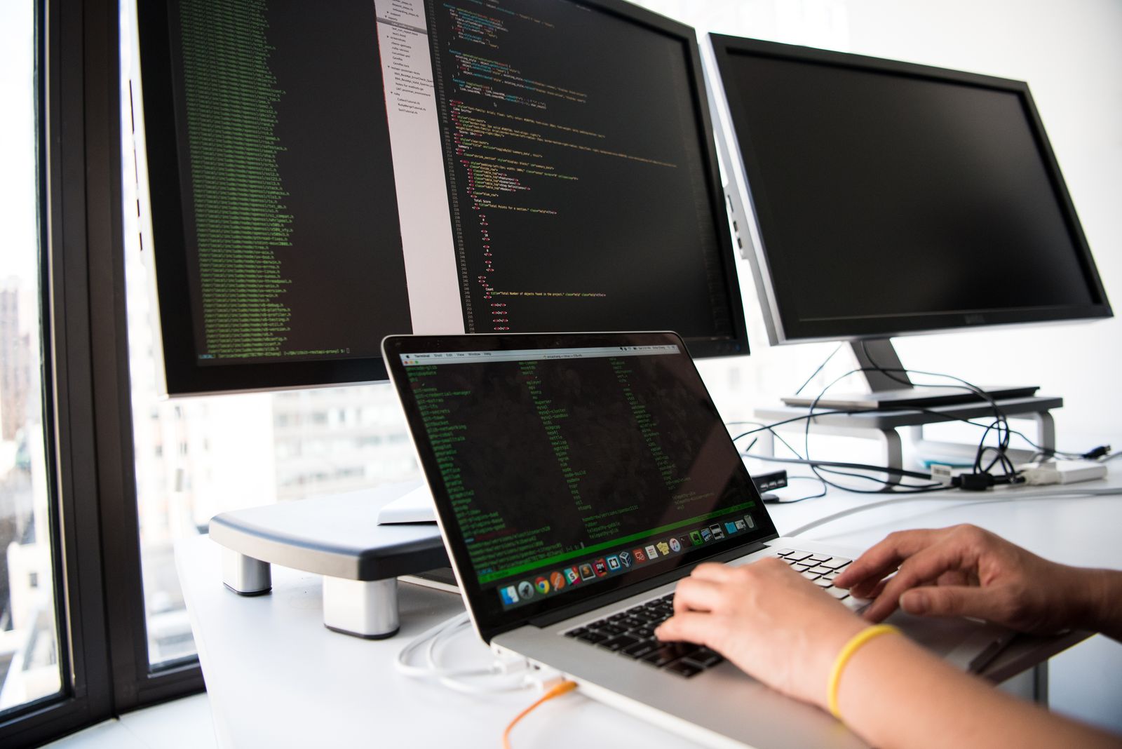 A developer writing code on a laptop connected to desktop monitors