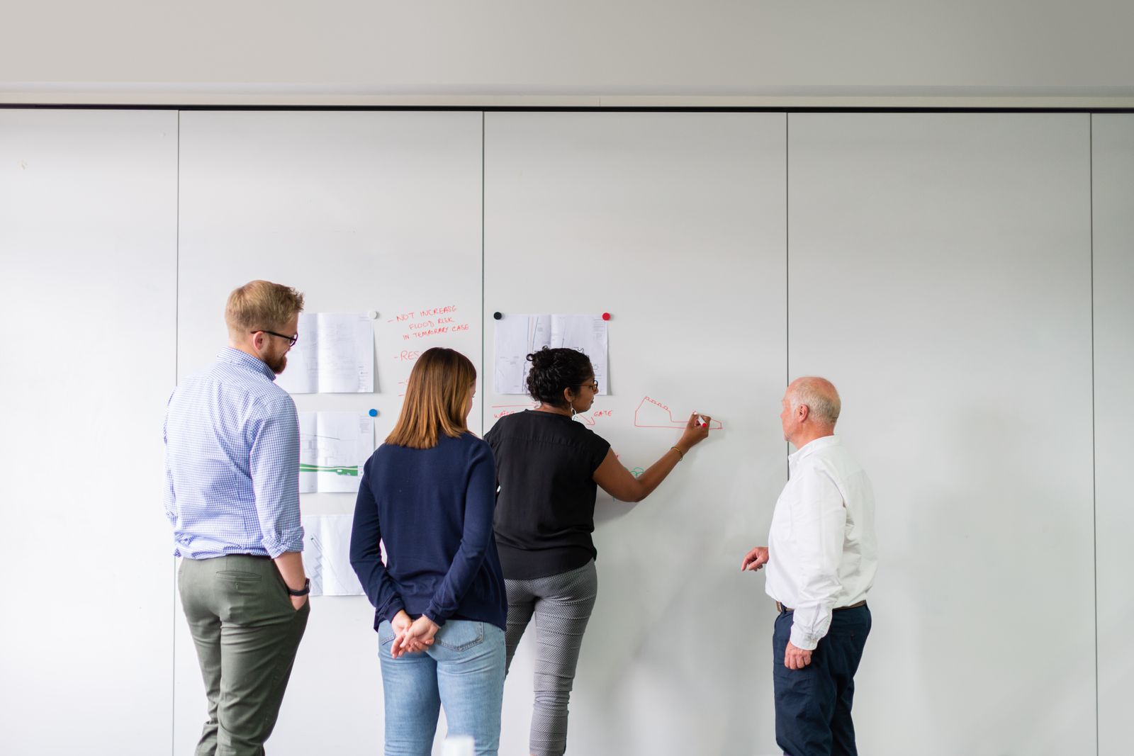 Four colleagues working through a technical plan on a large whiteboard